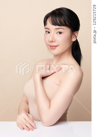 A beautiful young Asian woman with clean, fresh skin against a beige background. Skincare, facial treatment, cosmetology, beauty, and spa. An elegant portrait of an Asian woman. 129215729