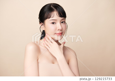 A beautiful young Asian woman with clean, fresh skin against a beige background. Skincare, facial treatment, cosmetology, beauty, and spa. An elegant portrait of an Asian woman. 129215733