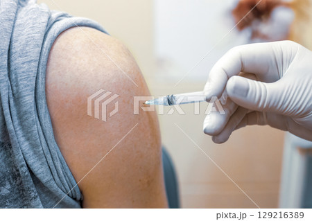 Doctor making flu injection in adult patient shoulder in clinic closeup. Hand holding syringe, making inject 129216389