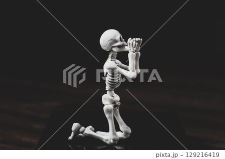 Pray skeleton figurine. Prayer figure on knees on dark background 129216419