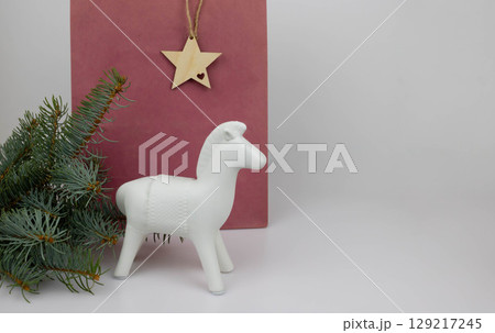 A red bag and a white ceramic horse stand on the table next to a bouquet of fir branches. The concept of New Year and Christmas 129217245