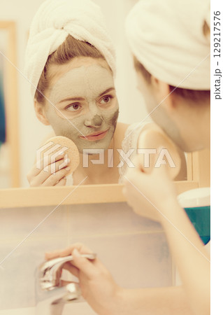 Woman removing facial clay mud mask in bathroom 129217576