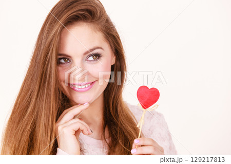 Flirty woman holding red wooden heart on stick Flirty woman holding red wooden heart on stick 129217813