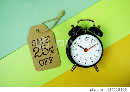 Sale 25% off text on price tag with alarm clock on green, yellow geometric background 129218196