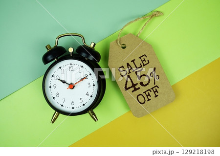 Sale 45% off text on price tag with alarm clock on green, yellow geometric background 129218198