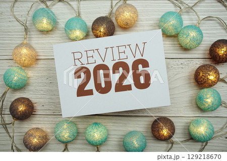 Review 2026 text on paper card with LED cotton balls top view on wooden background 129218670
