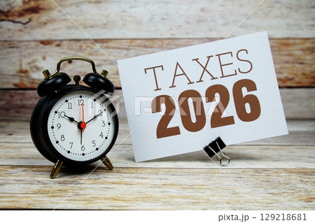 Taxes 2026 text with alarm clock on wooden background Taxes 2026 text with alarm clock on wooden background 129218681