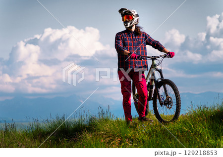 Portrait of a cyclist standing with his bicycle against a dramatic sky with cumulus clouds. Handsome young man biking in the countryside 129218853