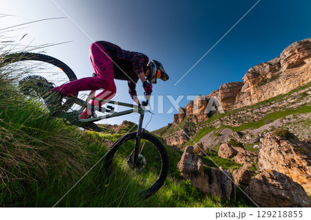 Mountain biker riding down a grassy slope. Enduro mountain bike. MTB against a mountain landscape Mountain biker riding down a grassy slope. Enduro mountain bike. MTB against a mountain landscape 129218855