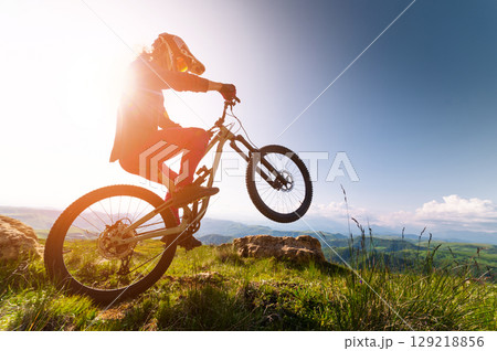 Young man riding through the air on a mountain bike on the back wheel. Fitness, extreme sports and mountain bike with man outdoors for cycling, jumping and adventure. Adrenaline junkie 129218856