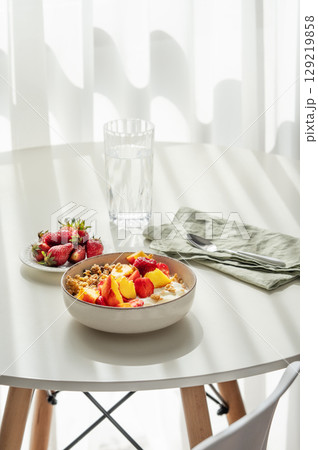 Granola or muesli with natural greek yogurt, strawberry and peach in a bowl on a white table Granola or muesli with natural greek yogurt, strawberry and peach in a bowl on a white table 129219858