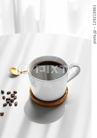 Freshly brewed espresso coffee in a cup on a white table near window with spoon, coffee beans 129219861