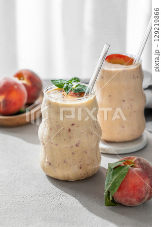 Two glasses of smoothie with peach and banana in a glass on a white table near window 129219866