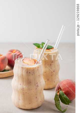 Two glasses of smoothie with peach and banana on a light background with tropical fruits. Two glasses of smoothie with peach and banana on a light background with tropical fruits. 129219868
