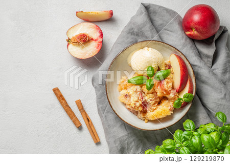 Peach crumble or cobbler with vanilla ice cream scoops and cinnamon on a plate on a light background 129219870