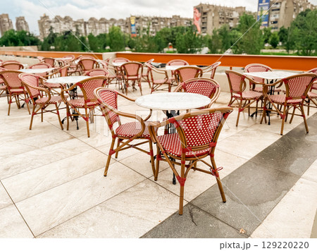 Outdoor cafe terrace with empty red chairs and round tables. Urban leisure, hospitality, and seasonal ambiance in a modern open-air dining area. Outdoor cafe terrace with empty red chairs and round tables. Urban leisure, hospitality, and seasonal ambiance in a modern open-air dining area. 129220220