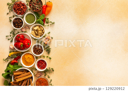 Assortment of vibrant spices and herbs on a warm beige background, showcasing a natural and aromatic palette for culinary inspiration, top view and copy space 129220912