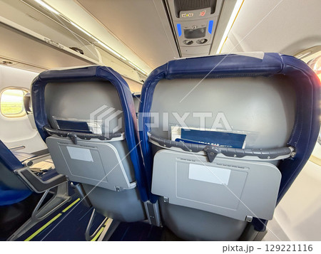 Airplane interior showing back of seats and cabin lighting. Travel routine, onboard details, and passenger environment during flight preparation. 129221116