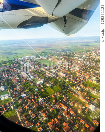 Aerial view of town and countryside from airplane window with engine visible. Urban planning, landscape diversity, and in-flight travel perspective. Aerial view of town and countryside from airplane window with engine visible. Urban planning, landscape diversity, and in-flight travel perspective. 129221125