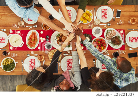 Christmas, high five and food with a group of friends sitting around a dinner table together for celebration. Thanksgiving, hands and meal with a team enjoying a lunch on a wooden surface from above 129221337