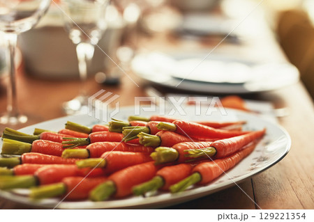 Thanksgiving, carrots and food with a plate of vegetables on a dinner table for tradition in an empty room. Roast, meal and nutrition with a lunch serving on a wooden surface in a house or home 129221354