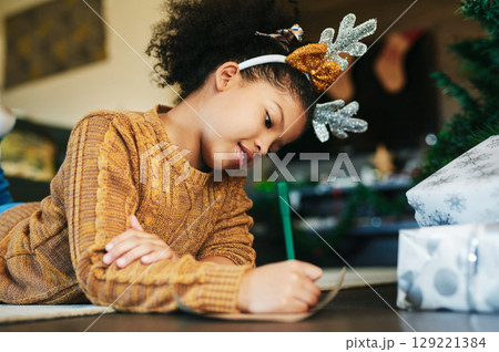 Child, christmas and writing letter, list of wishlist for gift or present from santa claus with hope to celebrate holiday with happiness at home. Girl kid with pencil to write note or xmas card 129221384
