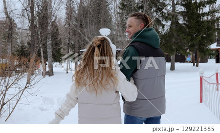 Young couple with dreadlocks walking in snowy park on winter day, enjoying each other's company and the beautiful scenery, wearing warm winter clothes 129221385