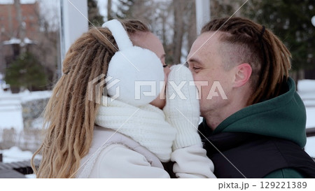 Loving couple embracing, sharing warm kiss amid snowy park landscape, winter outerwear protecting against chilly surroundings 129221389