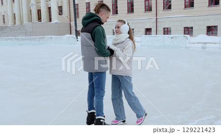 Romantic couple gliding hand in hand across frozen skating rink, sharing intimate moment during bright winter day, expressing deep connection and happiness outdoors 129221423
