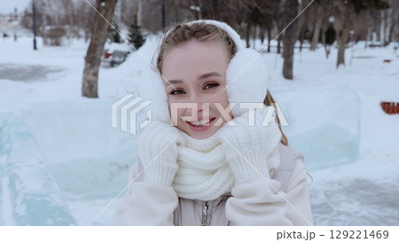 Young woman bundled in winter attire, smiling brightly while walking through snow covered park, radiating joy amid frosty landscape Young woman bundled in winter attire, smiling brightly while walking through snow covered park, radiating joy amid frosty landscape 129221469