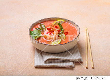 Traditional Thai soup tom yum soup with shrimp, lime, and herbs in bowl with chopsticks on light beige background 129221732