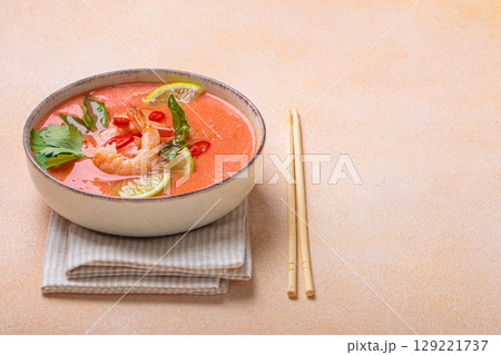Traditional Thai soup tom yum soup with shrimp, lime, and herbs in bowl with chopsticks on light beige background, space for text Traditional Thai soup tom yum soup with shrimp, lime, and herbs in bowl with chopsticks on light beige background, space for text 129221737