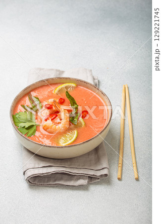 Traditional Thai soup tom yum soup with shrimp, lime, and herbs in bowl with chopsticks on light grey background 129221745