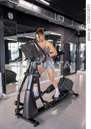 A woman is actively exercising on an elliptical machine at a modern gym facility 129221825