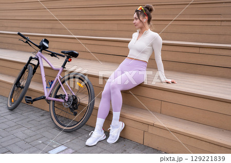 A Trendy Woman Dressed in Stylish Activewear is Enjoying a Relaxing Moment by Her Bicycle A Trendy Woman Dressed in Stylish Activewear is Enjoying a Relaxing Moment by Her Bicycle 129221839