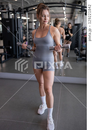 Beautiful young athletic girl in leggings and top crouches with dumbbells at modern gym. Sport, healthy lifestyle. Beautiful young athletic girl in leggings and top crouches with dumbbells at modern gym. Sport, healthy lifestyle. 129221842