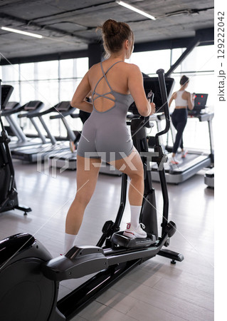 Woman training and fitness in gym on elliptical machine for health, wellness and cardio endurance. Cyclist, exercise bike and performance on equipment, power challenge and intense workout Woman training and fitness in gym on elliptical machine for health, wellness and cardio endurance. Cyclist, exercise bike and performance on equipment, power challenge and intense workout 129222042