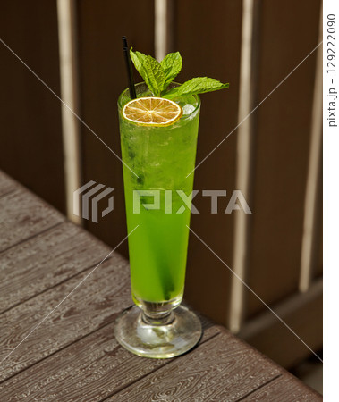 Refreshing green cocktail sitting on wooden table with lime and mint garnish Refreshing green cocktail sitting on wooden table with lime and mint garnish 129222090