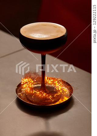 Espresso martini cocktail glass standing on a copper plate with sparkling christmas lights 129222115