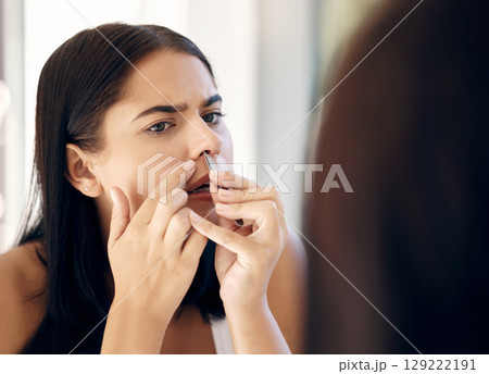 Face, nose and beauty with a woman using a tweezer to remove nasal hair in the bathroom of her house. Mirror, reflection and grooming with an attractive young female tweezing her nostrils at home Face, nose and beauty with a woman using a tweezer to remove nasal hair in the bathroom of her house. Mirror, reflection and grooming with an attractive young female tweezing her nostrils at home 129222191