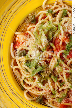 Delicious italian spaghetti with pesto, tomato sauce and capers being served on yellow plate 129222208