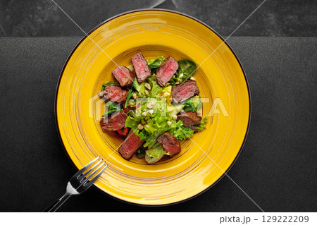 Warm salad with grilled medium-rare steak, lettuce, avocado, and nuts served on yellow plate Warm salad with grilled medium-rare steak, lettuce, avocado, and nuts served on yellow plate 129222209