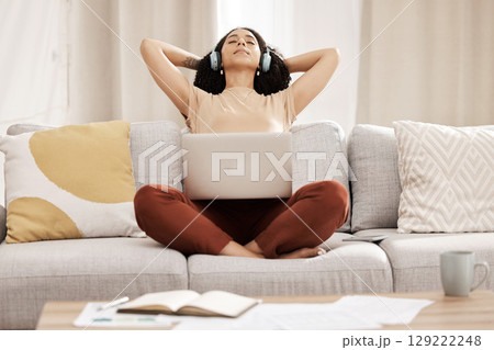 Black woman, headphones and laptop to relax, on couch for wellness and meditation in living room. Young female, girl and earphones for podcast, rest and on break for health, calm and peaceful on sofa Black woman, headphones and laptop to relax, on couch for wellness and meditation in living room. Young female, girl and earphones for podcast, rest and on break for health, calm and peaceful on sofa 129222248