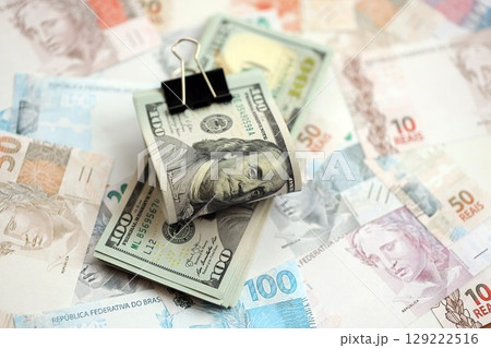 Bunch of US dollar bills lies on big amount of Brazilian reais banknotes close up Bunch of US dollar bills lies on big amount of Brazilian reais banknotes close up 129222516