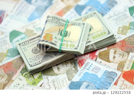 Bunch of US dollar bills lies on big amount of Pakistan rupees banknotes close up 129222558
