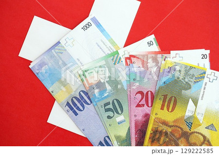 Swiss franc banknotes and flag. The current francs money bills lies on flag in big amount Swiss franc banknotes and flag. The current francs money bills lies on flag in big amount 129222585