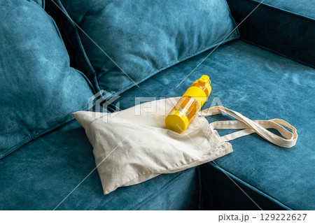 Reusable beige canvas shopping bag and yellow plastic bottle on sofa. Reusable beige canvas shopping bag and yellow plastic bottle on sofa. 129222627