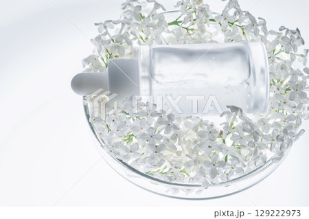 A bottle of serum in a petri dish with white flowers. A bottle of serum in a petri dish with white flowers. 129222973