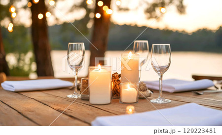 Candlelit dinner table with wine glasses beside a serene lakeside view 129223481