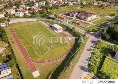Aerial view of a football field on a stadium covered with green grass in rural town area. Aerial view of a football field on a stadium covered with green grass in rural town area. 129223600